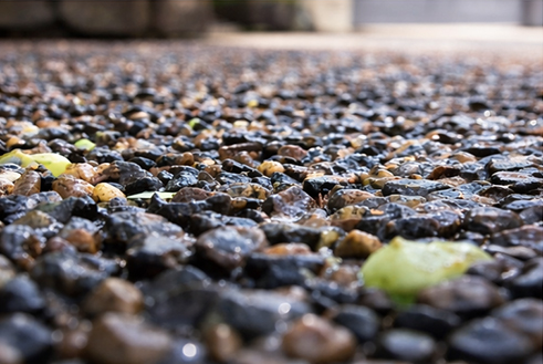 Close-up of wet permeable paving stones with a mix of small rocks and leaves.