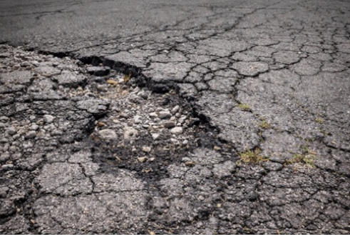 Close-up of cracked asphalt pavement with a pothole exposing gravel underneath.