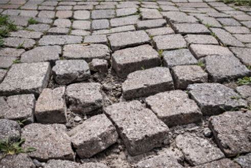 Close-up of uneven, cracked traditional stone paving with some grass growing between stones.
